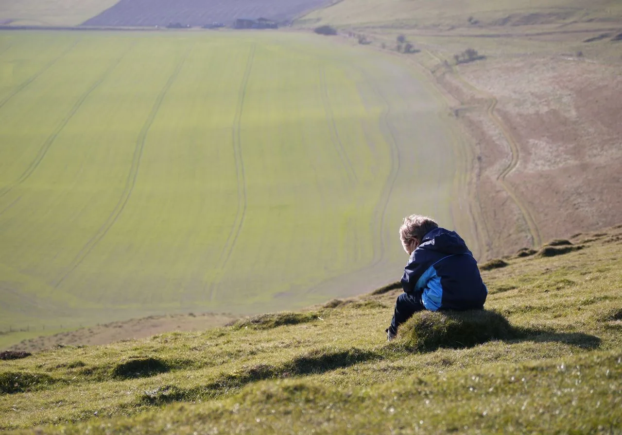 Seated kid facing away from camera facing vast farmlands